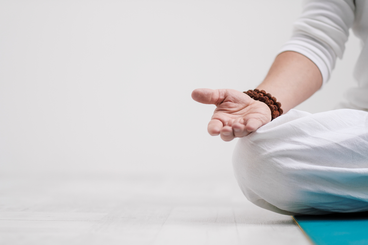 Concept of yoga and meditation. Close-up, hands of a man in white clothes, folded in prayer. White background and yellow-mini rubber mat. Copy space top view.