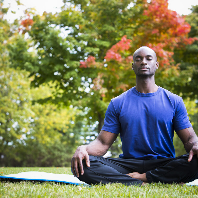young black man wearing athletic wear sitting in the park exercising yoga